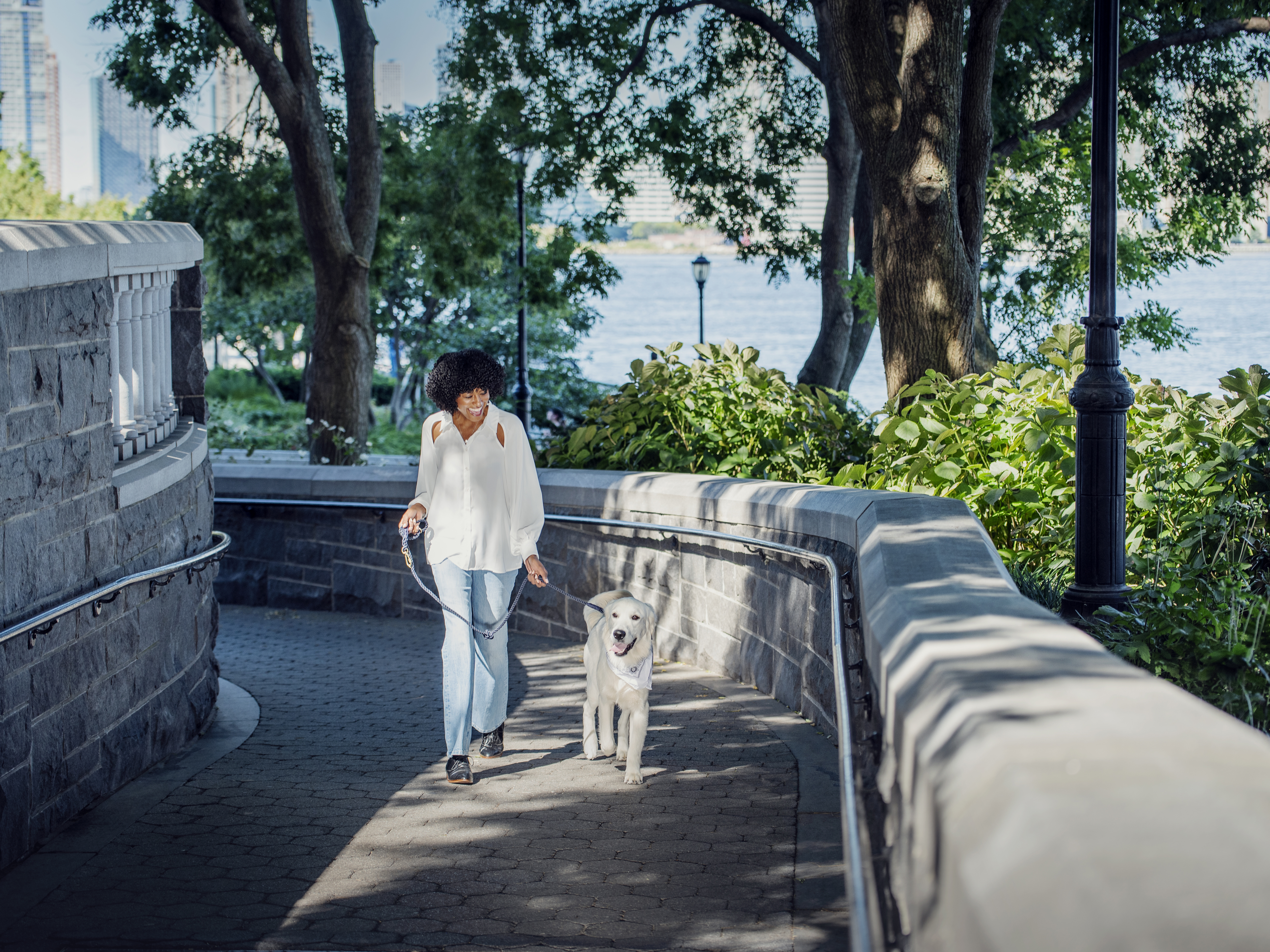 Woman walking with a golden retriever on a stone path in an urban park surrounded by trees